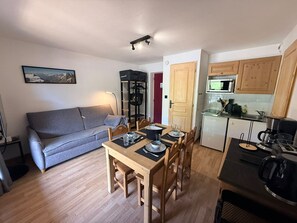 Ein gemütlicher, kompakter Wohnbereich mit Sofa, Esstisch, Stühlen, einer Küchenzeile und einem kleinen Fernseher.