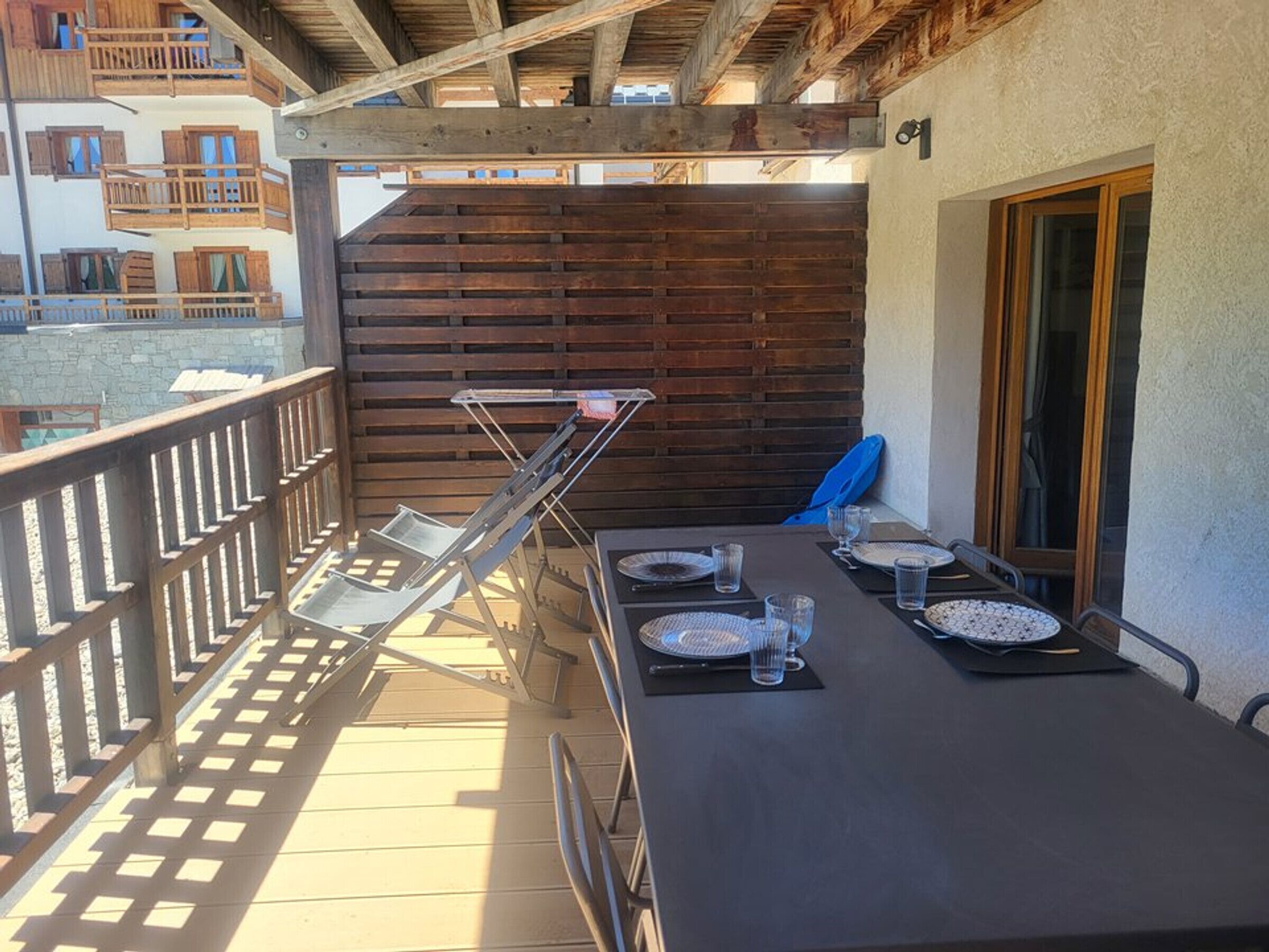 A balcony with a table set for two, a folding chair, and a wooden wall.