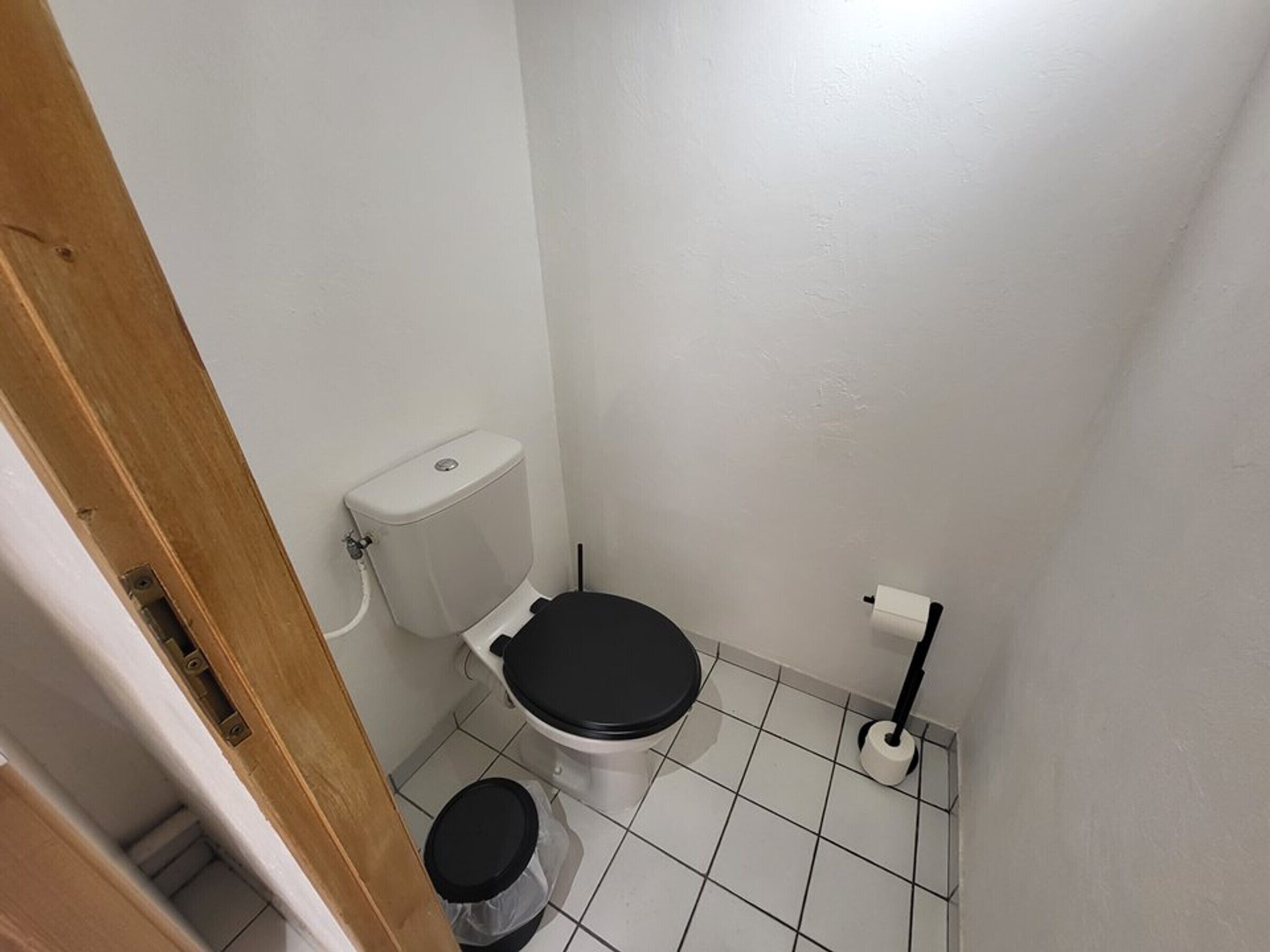 A small, clean bathroom with a toilet, a trash bin, and a toilet paper holder.