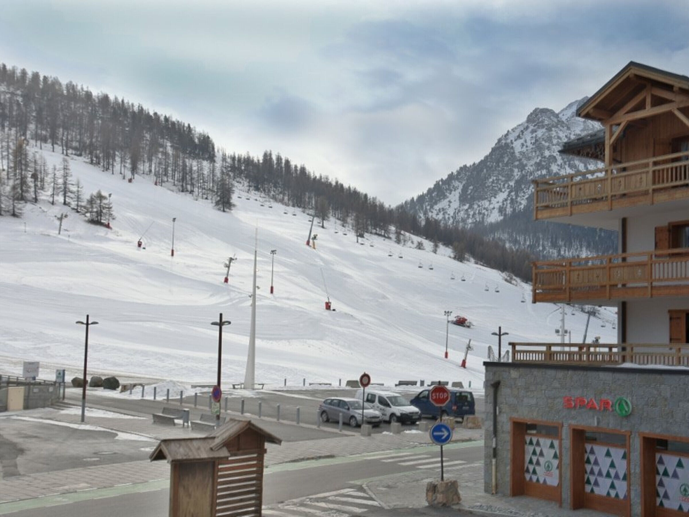 A ski resort with a wooden building, a ski lift, and a snowy mountain backdrop.