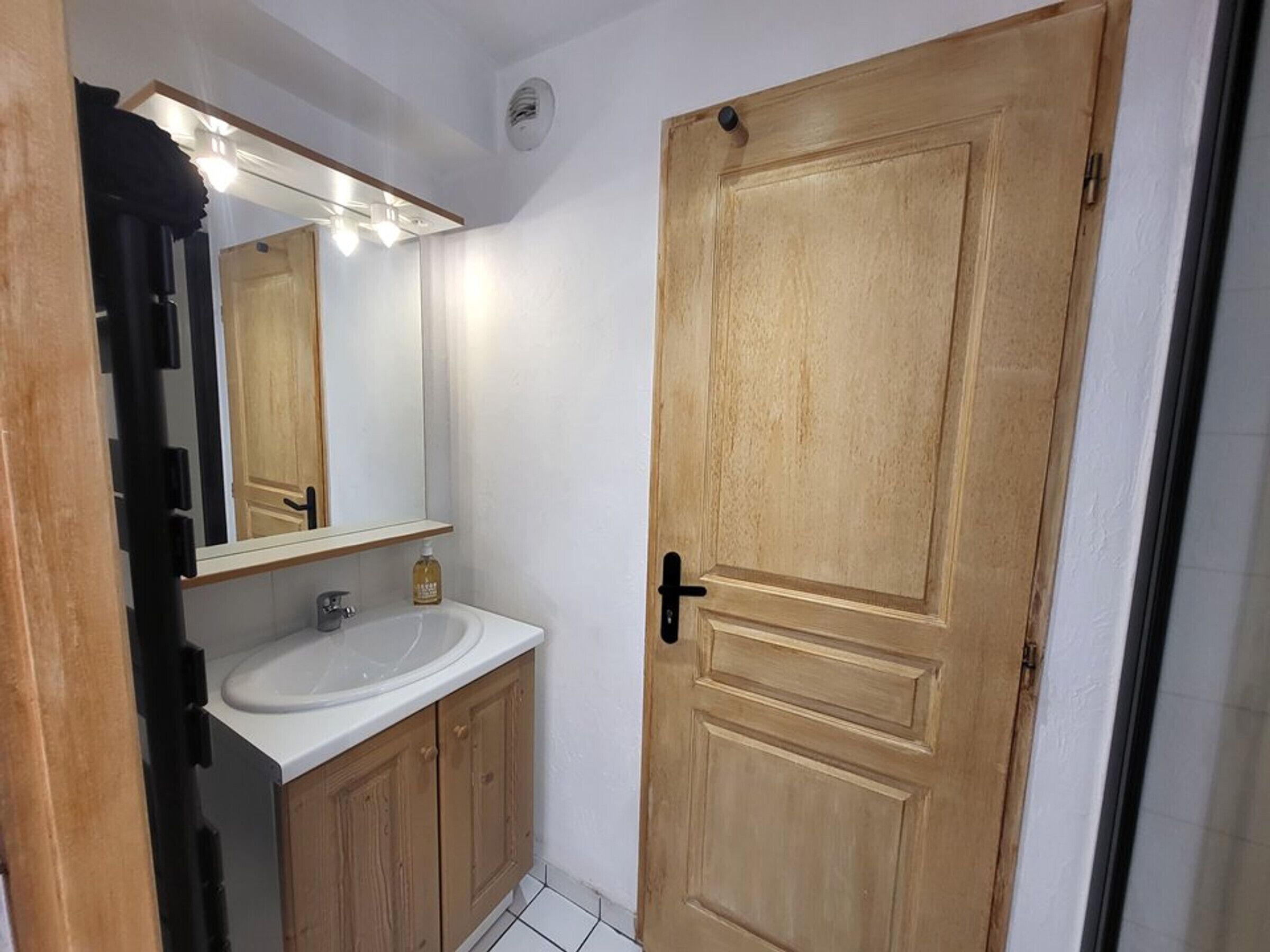 A bathroom with a wooden door, a white sink, and a mirror with lights.