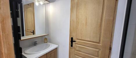 A bathroom with a wooden door, a white sink, and a mirror with lights.