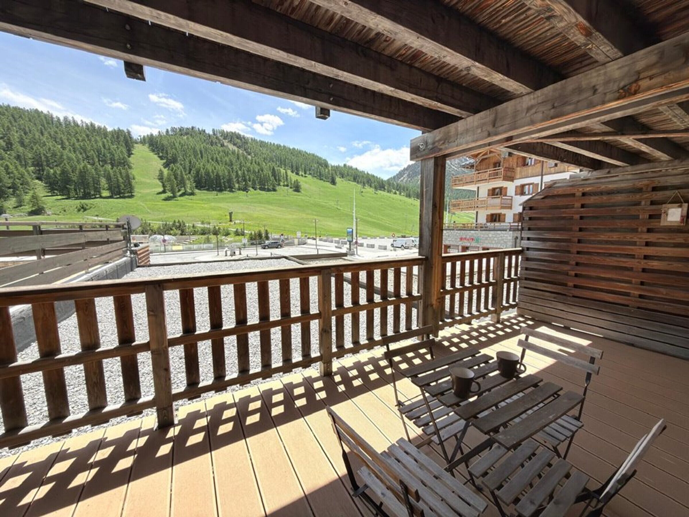 En träveranda med utsikt över en grönskande sluttning och en byggnad i bakgrunden.