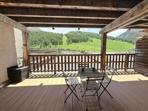 Eine Holzterrasse mit Tisch und Stühlen, mit Blick auf eine grüne Landschaft mit Bäumen und einem Berg.