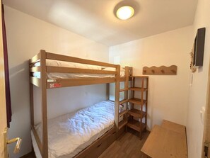 Ein Schlafraum mit einem Holzbett, einer kleinen Holzablage und einer Tür mit goldener Griff.