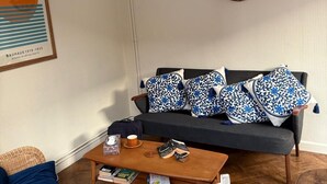 Uma sala de estar com sofá, mesa de centro, poltrona de vime e um quadro na parede.