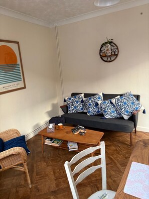 Ein Wohnzimmer mit einer Couch, einem Couchtisch, einem Korbstuhl und einem gerahmten Bild an der Wand.