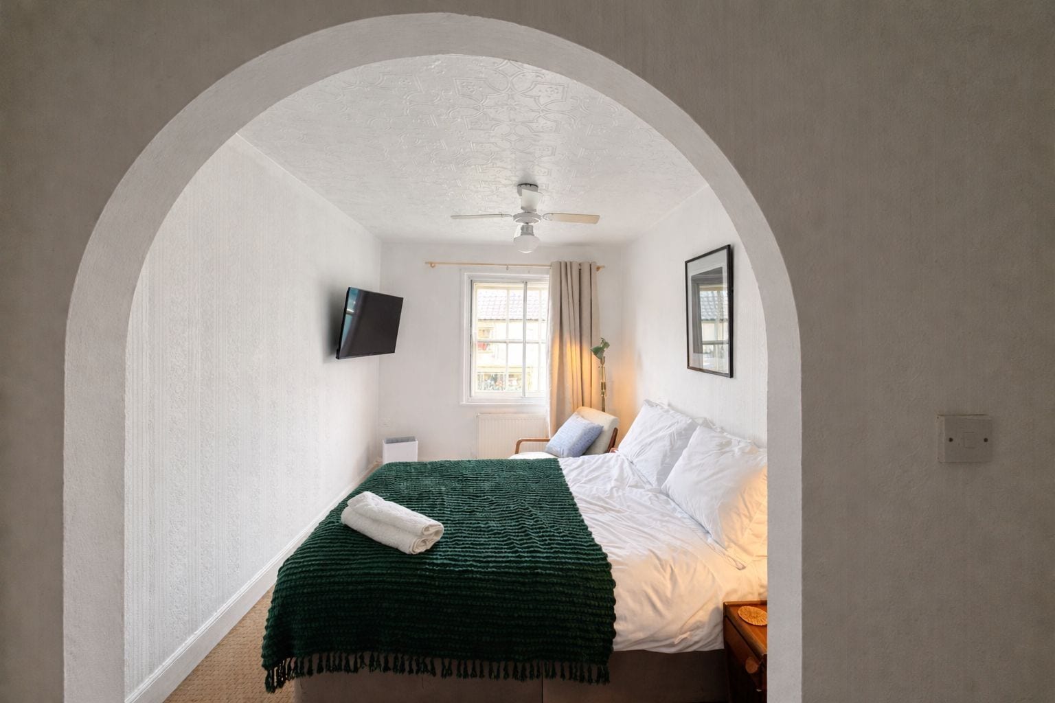 A bedroom with a bed, a television, a window, and an arched doorway.