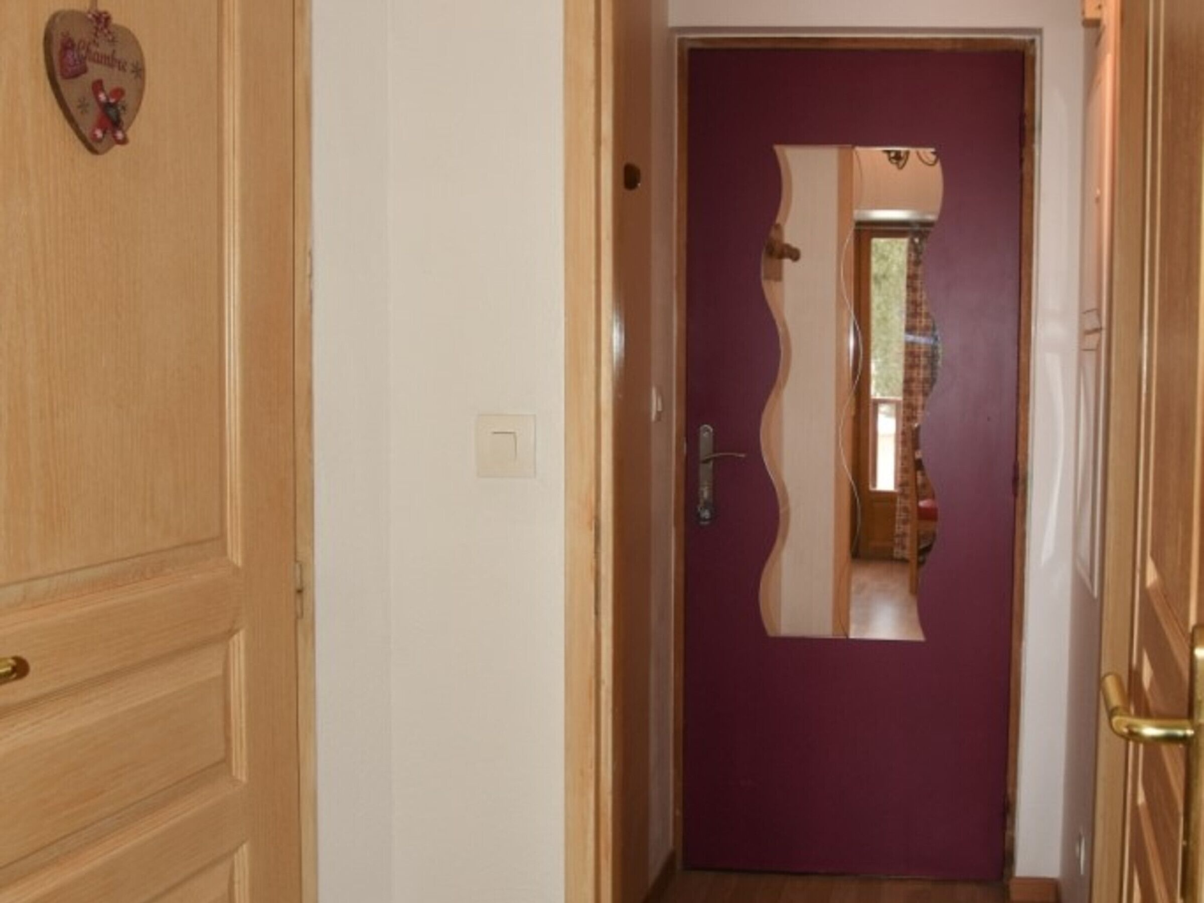 A hallway with a wooden door and a purple door with a mirror.