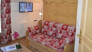 Een gezellige kamer met een houten slaapbank bekleed met een deken met een rood-wit patroon, een aan de muur bevestigde televisie en een houten deur met een messing knop.