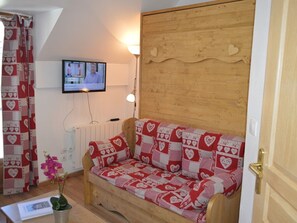 A cozy room with a wooden sofa bed covered in a red and white patterned blanket, a television mounted on the wall, and a wooden door with a brass handle. - Studio Montgenèvre view, pets welcome - 4 guests (Montgenèvre)