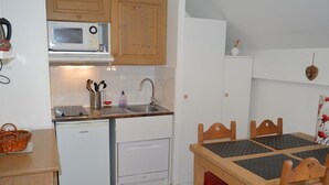 Een compacte keuken met een magnetron, spoelbak en vaatwasser. Er staat een eettafel met stoelen en een mandje op het aanrecht.