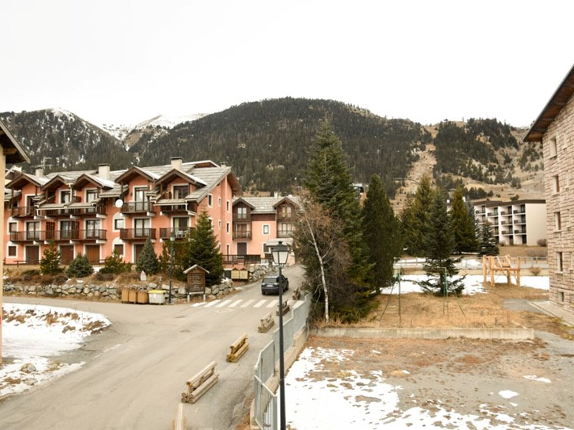 A multi-story hotel with balconies, a ski slope in the background, and a clear view of the mountains.