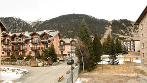Een hotel met meerdere verdiepingen en balkons, met een piste op de achtergrond en een helder uitzicht op de bergen.