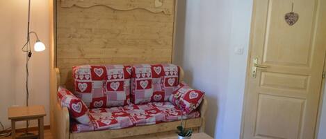 A cozy room with a wooden sofa adorned with heart patterns, a small wooden table, a lamp, and a door with a heart-shaped decoration.