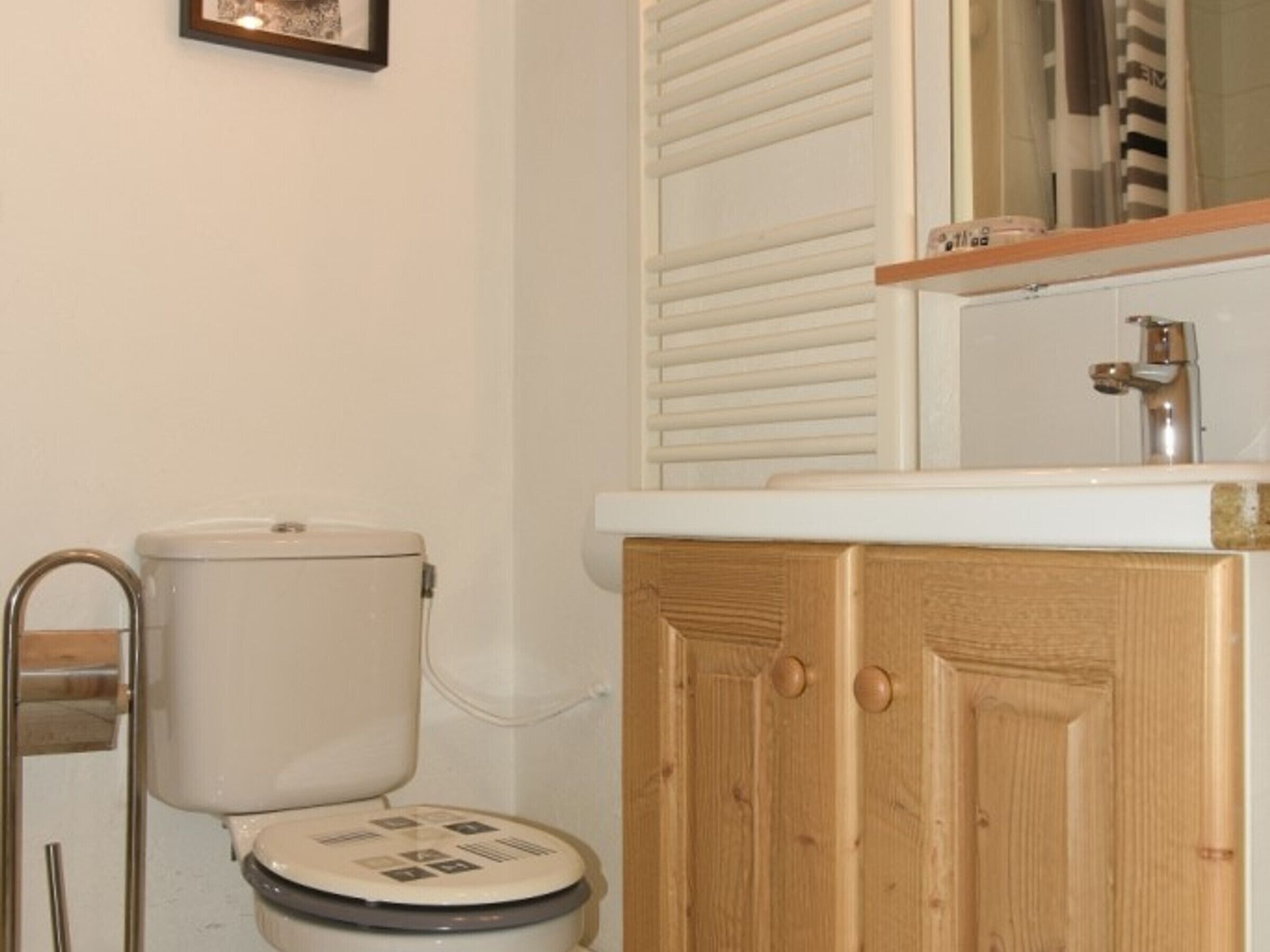 A bathroom with a toilet, wooden cabinet, and a mirror above the sink.