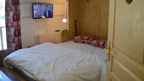 Een slaapkamer met een houten hoofdeinde, een aan de muur bevestigde televisie, een bedlamp en decoraties in de vorm van harten.