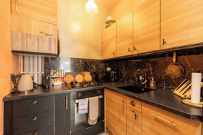 A modern kitchen with wooden cabinets, a black countertop, a stove, and a sink. - Modern 1BR Walk to Haymarket & Edinburgh Castle (Edinburgh)