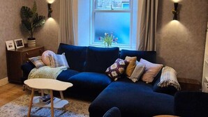 Un salón acogedor con un sofá azul oscuro, una mesa redonda de madera y una mesa de centro blanca.