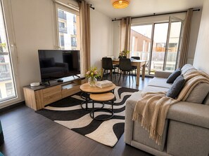 Un salon moderne doté d’un téléviseur à écran plat, d’un canapé, d’un coin repas et de grandes fenêtres.