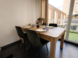 Un coin repas avec une table en bois dressée pour quatre personnes, des chaises, une plante en pot et une bouteille de vin.