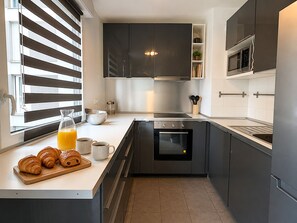 Eine moderne Küche mit dunklen Schränken, einem Einbauofen, einer Mikrowelle und einem Fenster mit Jalousien.