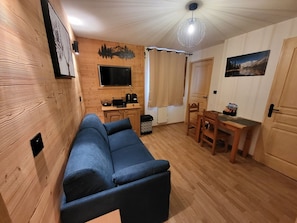 A cozy living area with a sofa, a dining table, and a TV. - Cozy studio facing the slopes, pets welcome (Montgenèvre)