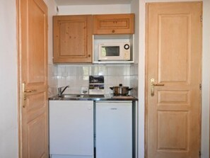 Eine kompakte Küche mit Holzausstattung, einer Mikrowelle, einem kleinen Kühlschrank und einem Herd.