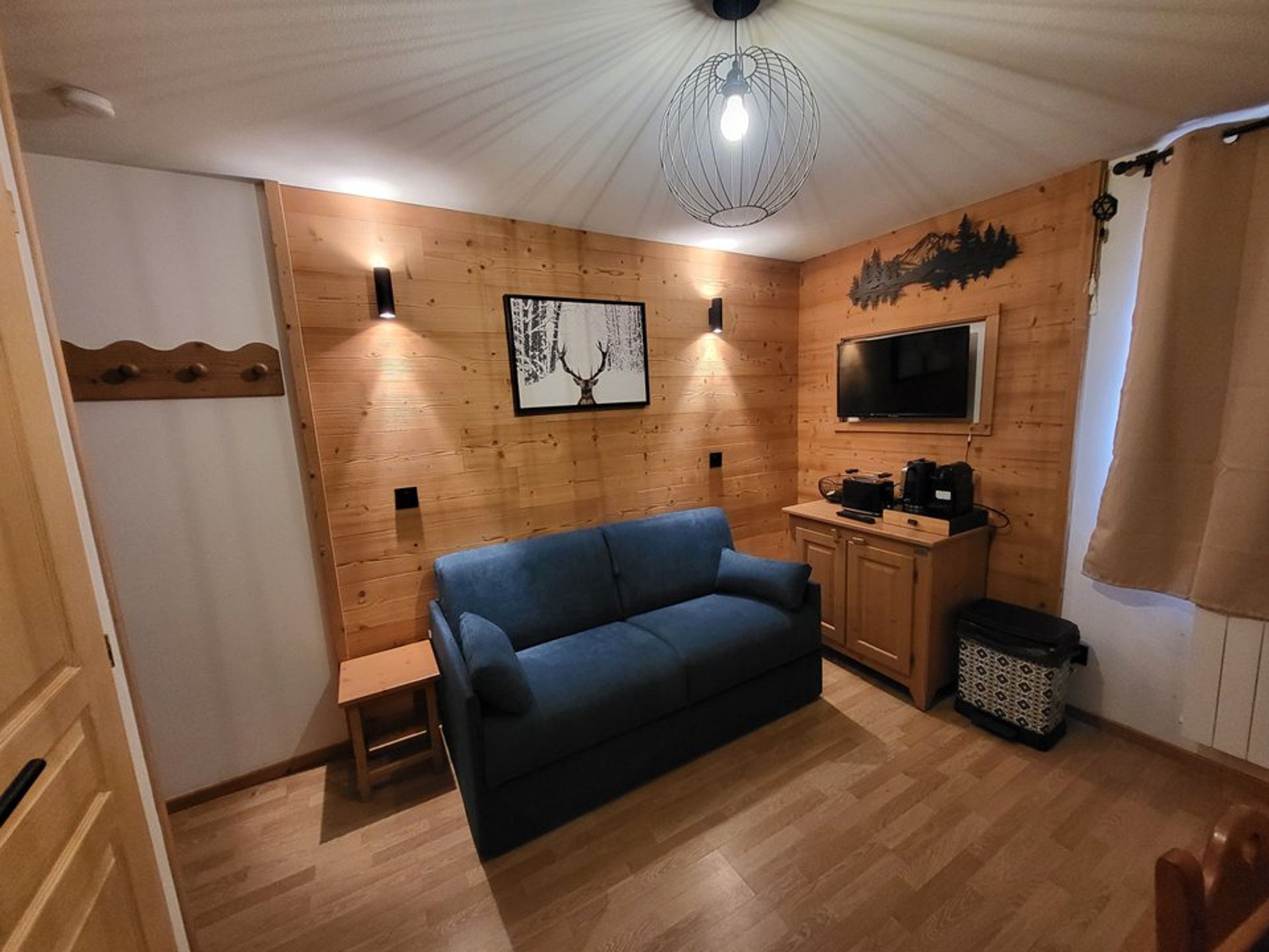 Ein gemütliches Zimmer mit einem blauen Sofa, Holzwänden, einem an der Wand befestigten Fernseher und einer Deckenleuchte.