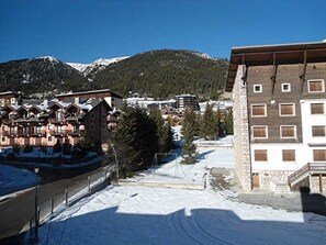 Ein schneebedecktes Skigebiet mit traditionellen Chalets, wolkenlosem Himmel und einem Berg im Hintergrund.