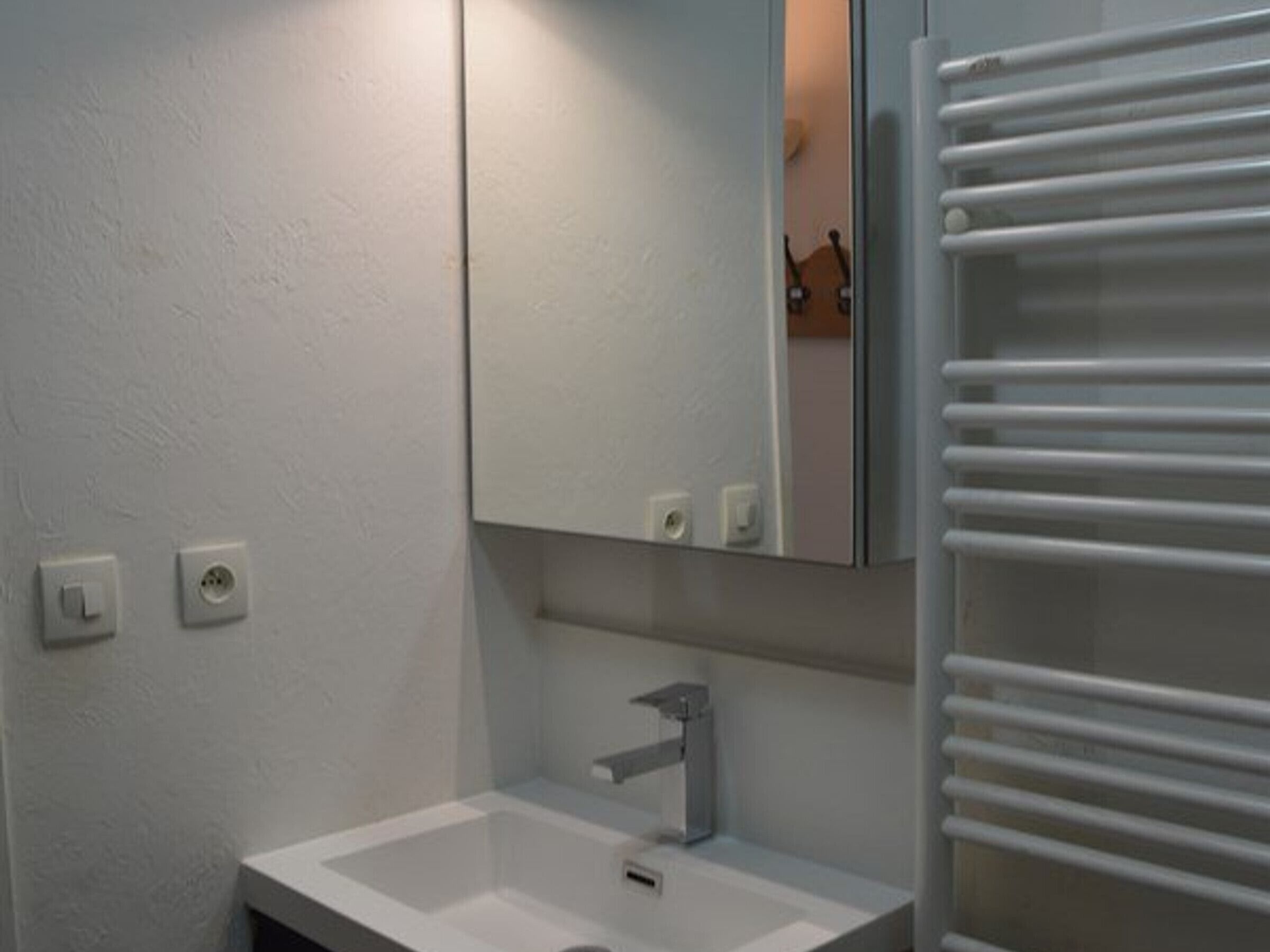 Casa de banho com uma pia branca, espelho e porta-toalhas.