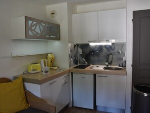 Eine kleine Küche mit weißen Schränken, einem Spülbecken und einer Arbeitsplatte. Auf der Arbeitsplatte befinden sich ein gelber Toaster und eine Kaffeemaschine.