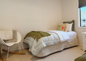 A bedroom with a bed, a chair, a nightstand, and a window.