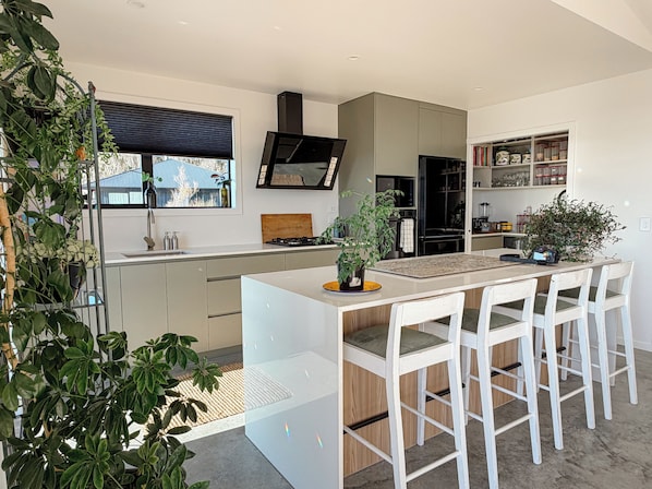 A modern kitchen with a central island, bar stools, and a window with blinds.
