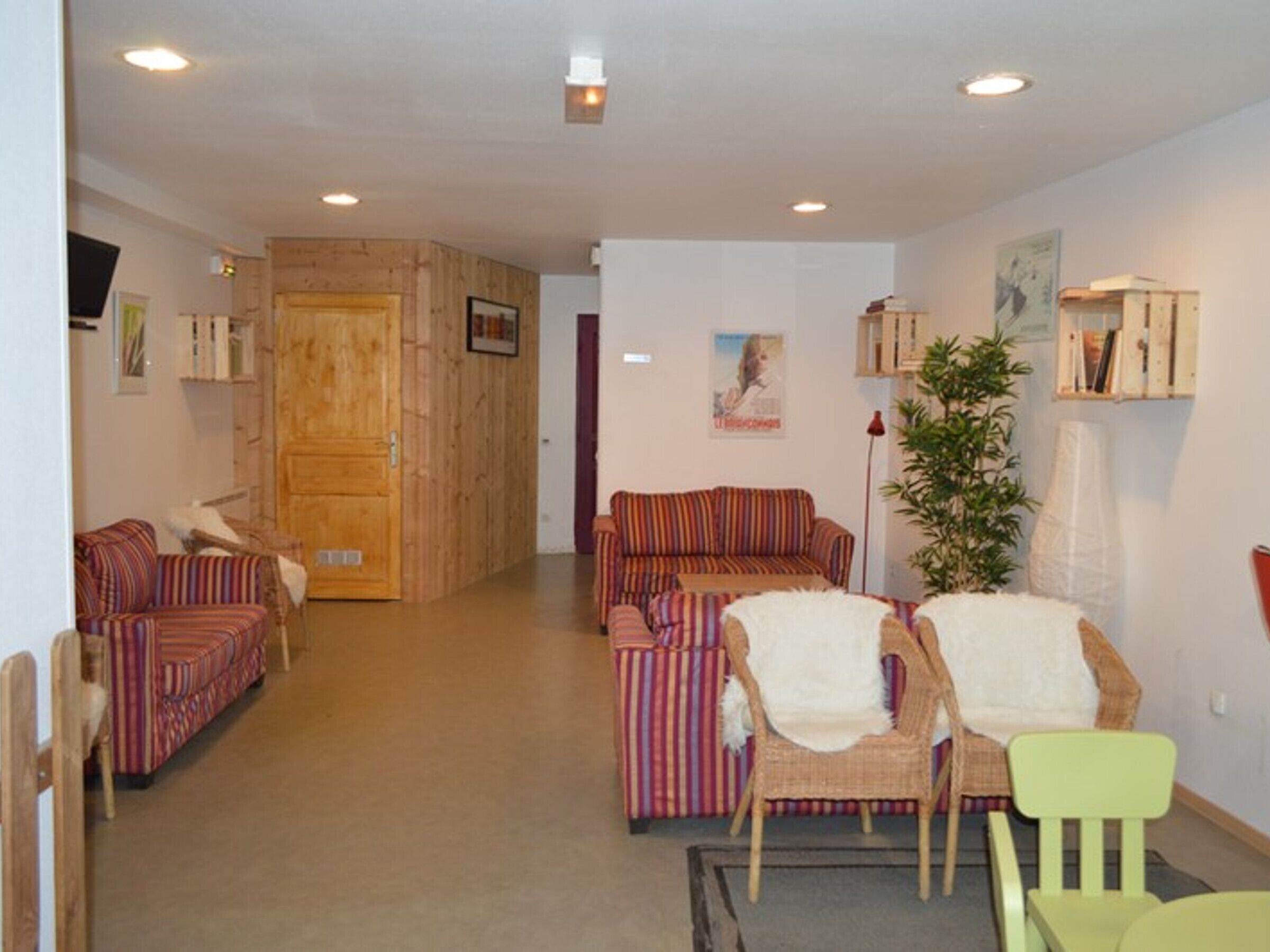 Ein Wohnzimmer mit gestreiften Sofas, einem grünen Sessel, einer Holztür und einer Pflanze.