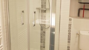 A glass-enclosed shower with a patterned tile border, a metallic faucet, and a toilet with a red pipe. - Cozy studio, mountain view (Montgenèvre)