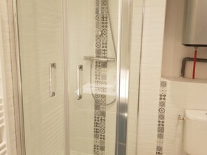 Eine gläserne Dusche mit gemusterten Fliesen an der Kante, einem metallenen Wasserhahn und einer Toilette mit einer roten Leitung.