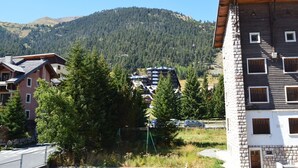 A multi-story building with a stone facade and multiple windows, surrounded by greenery and a mountainous backdrop. - Cozy studio, mountain view (Montgenèvre)