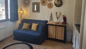 A living room with a blue sofa, a wooden cabinet, a wall clock, and decorative wall art. - Cozy studio, mountain view (Montgenèvre)
