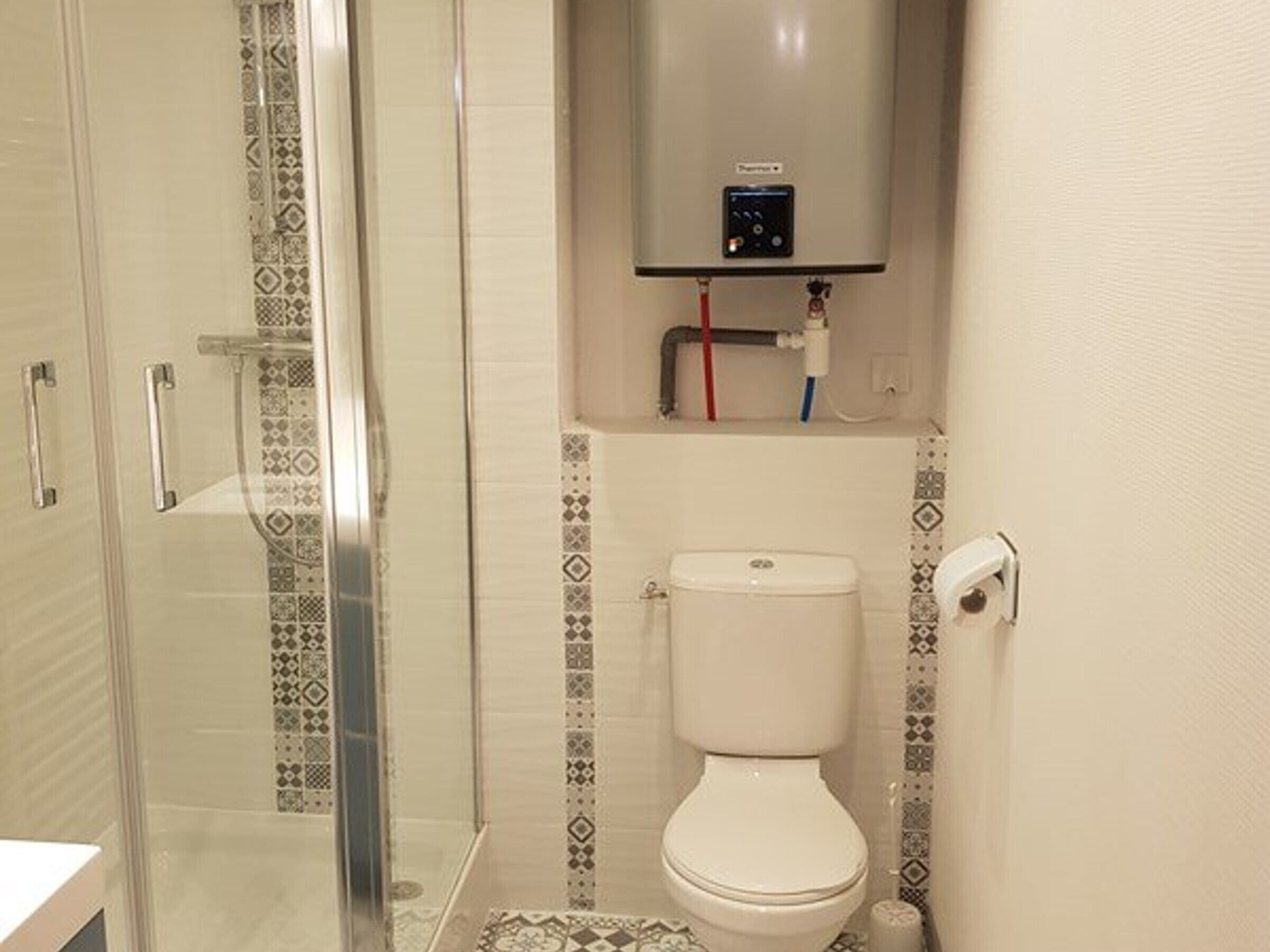 A bathroom with a glass shower enclosure, a toilet, and a wall-mounted control panel.