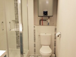 Casa de banho com cabine de duche em vidro, sanita e painel de comando fixado na parede.