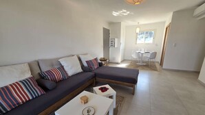 A modern living room with a sectional sofa, a small white table, and a dining area in the background. - Apartment sea view, AC - 4 guests (Lumio)