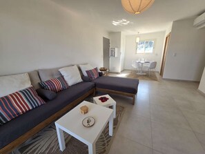 A modern living room with a sectional sofa, a small white table, and a dining area in the background. - Apartment sea view, AC - 4 guests (Lumio)