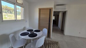 A modern room with a round table and four chairs, a wooden door, and a view of greenery outside. - Apartment sea view, AC - 4 guests (Lumio)