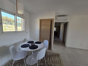 A modern room with a round table and four chairs, a wooden door, and a view of greenery outside. - Apartment sea view, AC - 4 guests (Lumio)