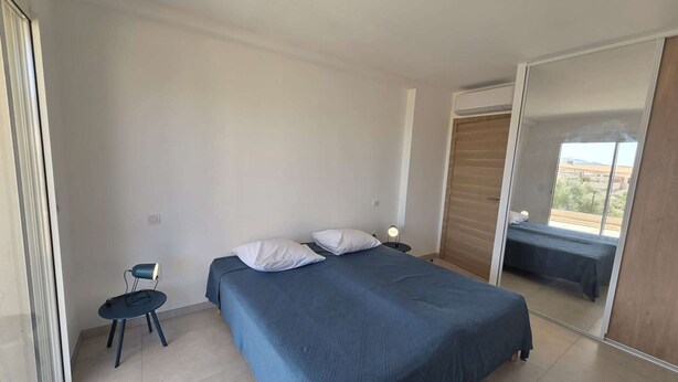 A bedroom with a bed, a chair, a nightstand, and a large mirror. - Apartment sea view, AC - 4 guests (Lumio)