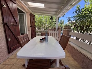 A covered patio with a white table and wooden chairs, a bottle, and a mug on the table. - House with parking - 5 guests (Saint-Cyprien)