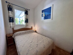 A bedroom with a bed, a nightstand, a window with curtains, a wall-mounted picture, and a wooden floor. - House with parking - 5 guests (Saint-Cyprien)