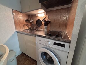 Ett kompakt kök med tvättmaskin, diskho och ett förvaringsställ för köksredskap.
