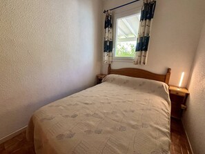 A single bed with a patterned bedspread, a nightstand, a lamp, and a window with curtains. - House with parking - 5 guests (Saint-Cyprien)
